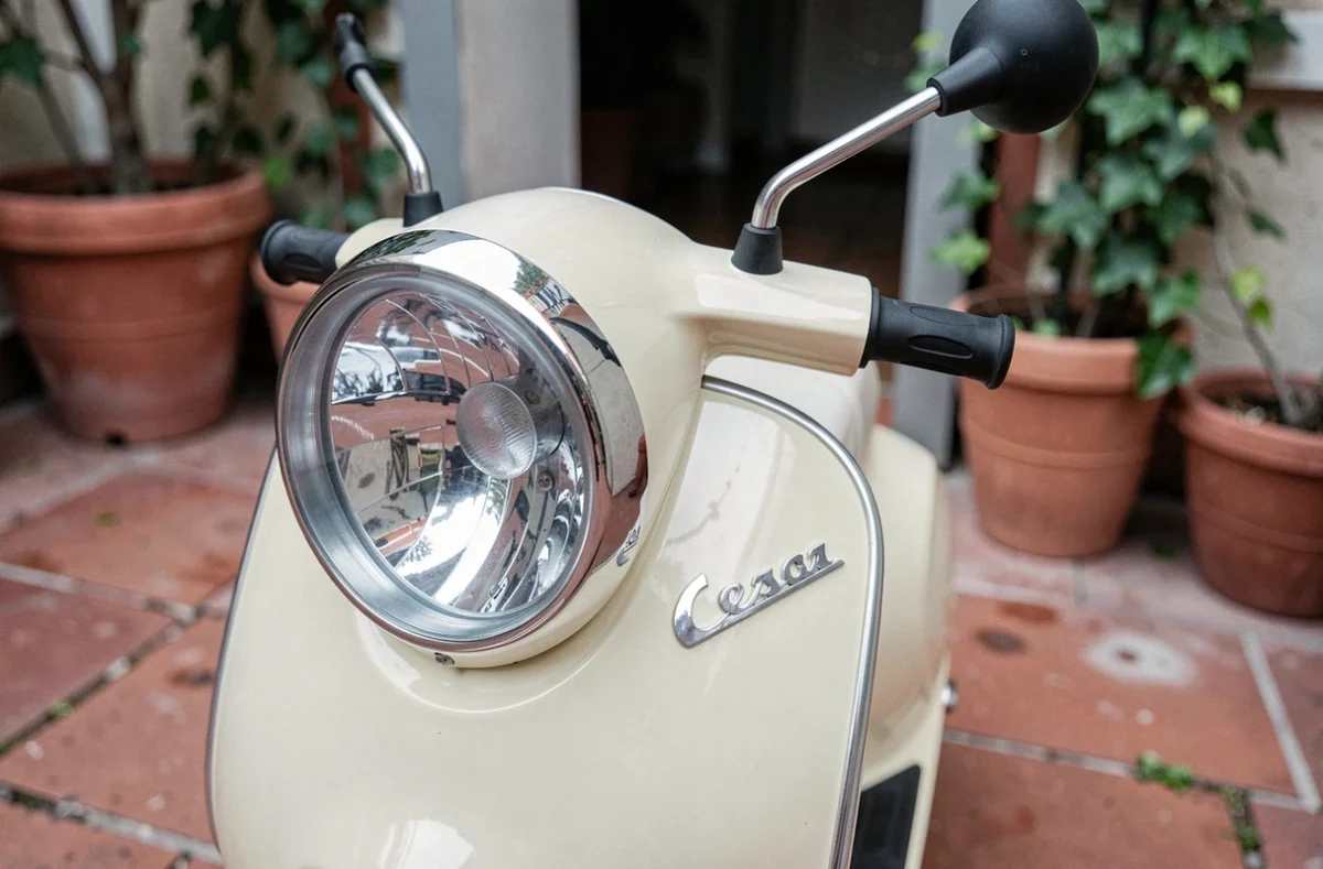 Détail du phare et du carénage chromé d'un scooter bébé électrique style Vespa sur carrelage terracotta